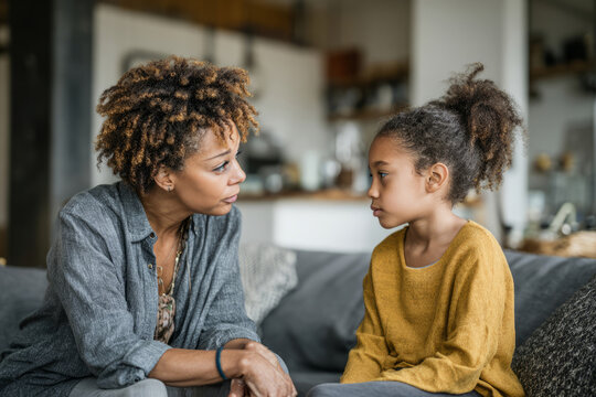 Woman and girl sitting on couch at home and having a serious conversation - Powered by Adobe