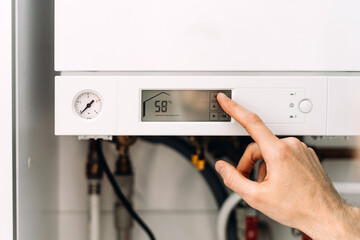 Naklejka na ściany i meble Repairman adjusting digital control panel on gas boiler in bathroom for heating Naklejka na ściany i meble Repairman adjusting digital control panel on gas boiler in bathroom for heating