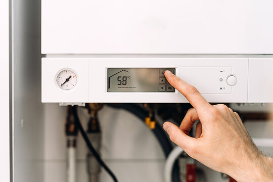 Repairman adjusting digital control panel on gas boiler in bathroom for heating