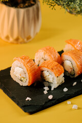 Fresh sushi rolls served on slate board with yellow background and decorative plant
