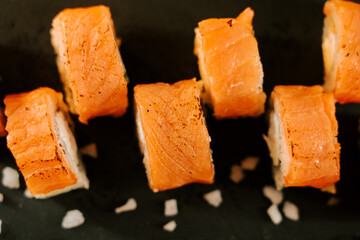 Freshly prepared salmon sushi rolls arranged neatly on a black plate with garnishes