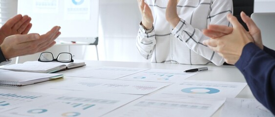 Business team clapping hands in meeting celebrating success with financial charts, data analysis, sales growth reports, and teamwork achievement in modern office
