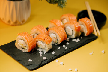 Delicious sushi rolls served on a black stone plate with chopsticks and salt crystals