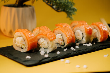 Delicious sushi rolls served on a black stone plate with a vibrant yellow backdrop