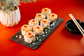 Sushi rolls served on a black slate plate with chopsticks and a dipping sauce