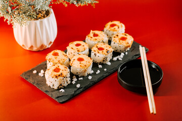 Delicious sushi rolls arranged on a black stone platter with soy sauce and chopsticks beside them