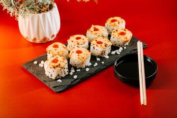 Brightly colored sushi rolls served on a black stone plate with sauces and chopsticks