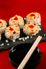 Unique sushi rolls on a black stone plate with soy sauce and chopsticks resting nearby