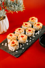 Unique sushi rolls with vibrant red toppings arranged on a dark slate plate