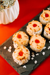 Unique sushi dishes topped with a spicy sauce served on a black slate plate