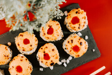 Sushi rolls topped with sauce served on a dark plate in a vibrant restaurant setting