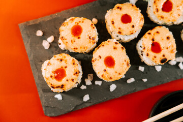 Delicious sushi rolls topped with sauce on a black plate against a vibrant background
