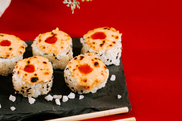 Delicious sushi rolls with melted topping served on a black plate against a red background