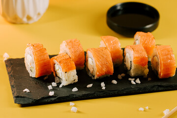Sushi rolls served on a slate platter against a bright yellow background