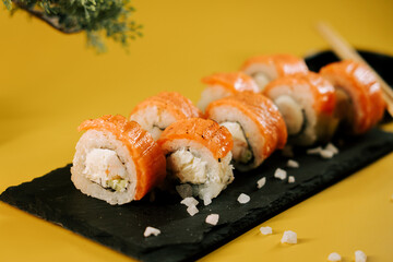 Fresh sushi rolls placed on a black slate plate with a yellow backdrop