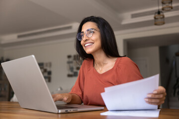 Cheerful young Latin freelance accountant woman working on paper reports
