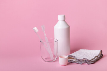White toothbrushes in glass, mouthwash and face towel  on pink background. Oral care, gum and teeth health. Morning routine and dental care.