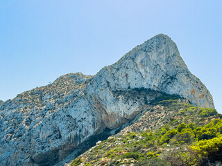 Majestic rocky mountain peak under clear blue sky with greenery in the foreground and sunny weather shining brightly