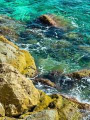 Bright turquoise waves crash gently against rocky shores, revealing the beauty of nature under the sun at midday along a serene coastal landscape