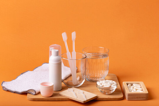 White toothbrushes in glass, dental floss, mouthwash on wooden desk, toothpaste and face towel on orange background. Oral care, gum and teeth health. Morning routine and dental care.