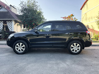 Black SUV parked on a sunlit street surrounded by trees and residential homes in a peaceful...