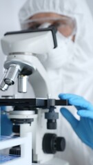 Scientific researcher or virologist wearing protective gear adjusting microscope, analyzing lab samples with precision in sterile research environment. Medicine and science concept