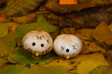 Two mushrooms with carved faces on autumn leaves and orange background. Creative idea for Halloween and fall decorations.