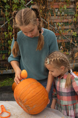 Young girl and child engaged in pumpkin carving activity outdoors, showcasing creativity and teamwork while preparing for autumn festivities with vibrant orange pumpkins