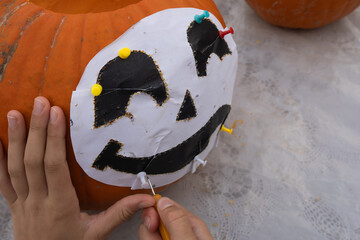 Child's hand carefully carving a pumpkin with a playful face design using a small knife, showcasing creativity and festive spirit in autumn decoration