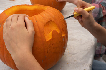 Hands of children carving a pumpkin with a small knife, showcasing creativity and fun during autumn festivities, highlighting the joy of seasonal traditions and craftsmanship