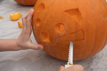 Child's hand carving a pumpkin with a playful cat face design, showcasing creativity and seasonal festivities in a cozy, inviting atmosphere