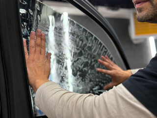 Applying tinting foil on a car window in the tuning studio close-up. Male car service worker glue window tinting in luxury car detailing car repair the concept of love for cars and protection. 