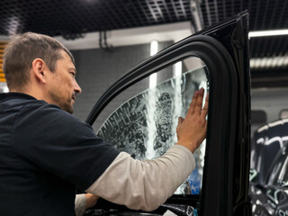 Applying tinting foil on a car window in the tuning studio close-up. Male car service worker glue...
