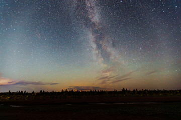 Night sky filled with stars and the Milky Way galaxy, showcasing a breathtaking cosmic view over a serene landscape with silhouettes of trees and distant mountains