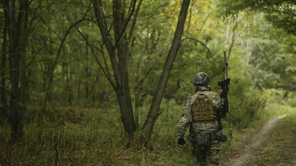 Camouflaged and masked army soldier with AR15 carbine on a mission. Carefully sneaking through a thick green forest. Military recon