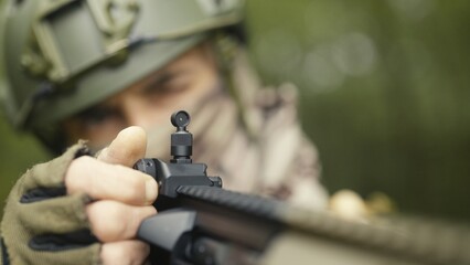 Camouflaged and masked army soldier with AR15 carbine. Rifle with a collimator aiming at the camera. Selective focus. Military recon