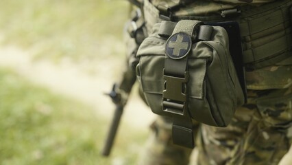 Camouflaged army soldier on a stealth mission. Close-up on the military equipment with first aid kit. Military recon