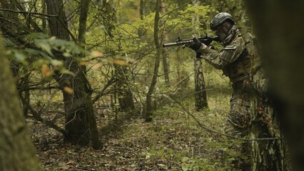 Camouflaged army soldier with AR15 carbine on a mission. Traversing the rough terrain of trees and bushes. Military recon