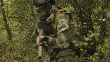 Camouflaged army soldier with AR15 carbine on a mission. Traversing the rough terrain of trees. Military recon