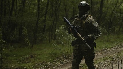 Camouflaged and masked army soldier with AR15 carbine on a war recon mission. Walking through the lush forest. Military recon