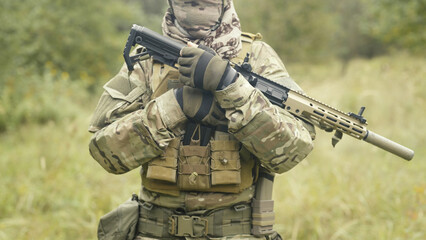 Camouflaged and masked army soldier with AR15 carbine on a war recon mission. Holding the gun close. Military recon