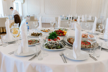 Elegantly set round banquet table with appetizers, white linens, crystal glasses, and neatly folded napkins for a formal reception