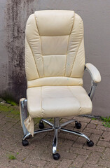 brown leather office chair stands outside on the street next to a plastered wall