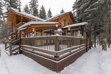 A charming wooden cabin nestled in a snowy forest showcases warm lanterns illuminating the...