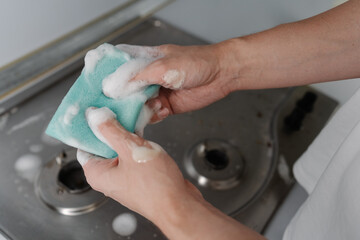 Cleaning company worker squeezing soapy water from sponge during cleaning dirty gas stove, to removing grime, grease, promoting hygiene, cleanliness in kitchen. Concept of domestic work, household.