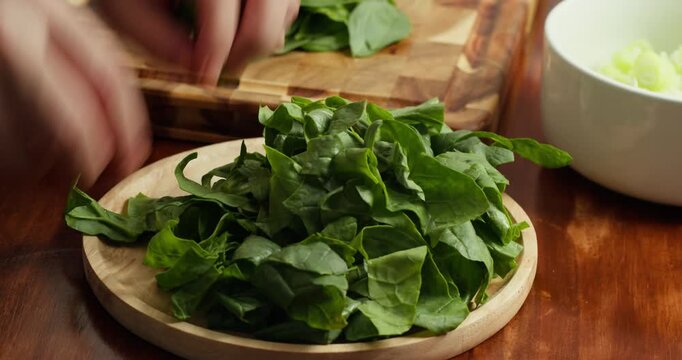 Close up of person cutting fresh spinach on wooden board, preparing ingredients for healthy vegan meal, organic cooking process, green vegetables, rustic kitchen atmosphere, natural lifestyle.