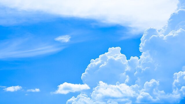 Vibrant blue sky with large, towering cumulus clouds on the right and wispy cirrus clouds, creating a vast and majestic aerial backdrop.
