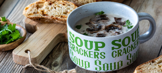A narrow view of a cup of cream of mushroom soup served with crusty bread.