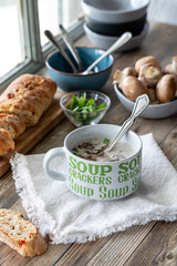 Above view of a cup of cream of mushroom soup with bread, next to a window.