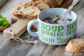 A cup of cream of mushroom soup served with a crusty baguette.